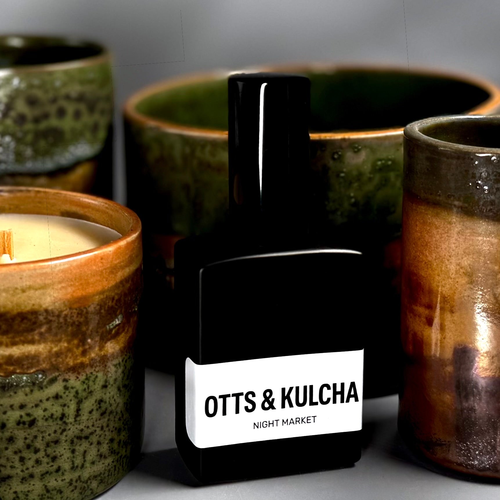 Black perfume bottle with 'Ott's & Kulcha' label among ceramic containers
