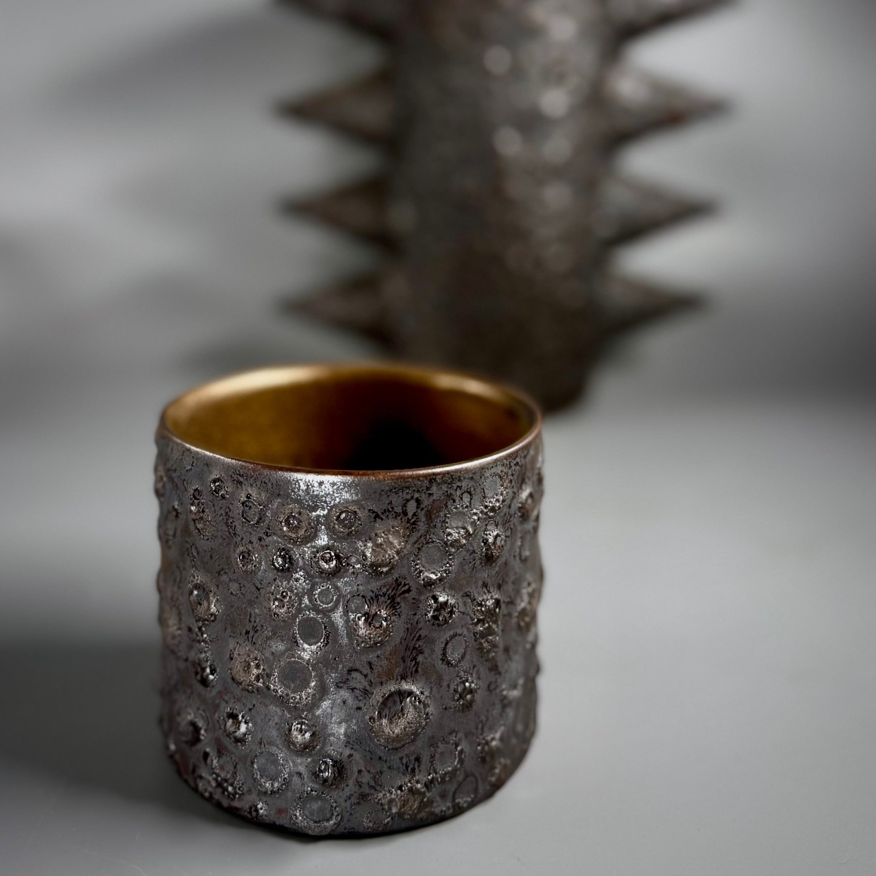 Textured metal cup with a spiky object in the background on a gray surface