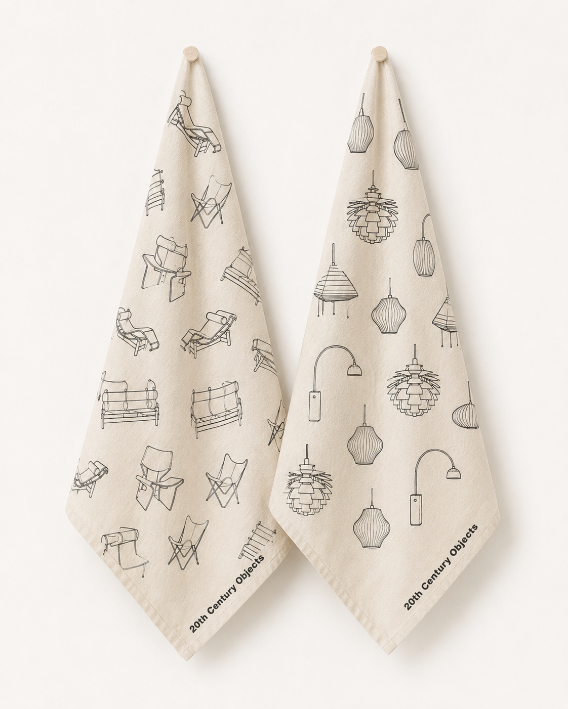 Two cream-colored cotton kitchen towels hanging from wooden pegs against a white wall. The towels feature black line-art illustrations of 20th-century furniture and lamps, with the text '20th Century Objects' printed at the bottom.